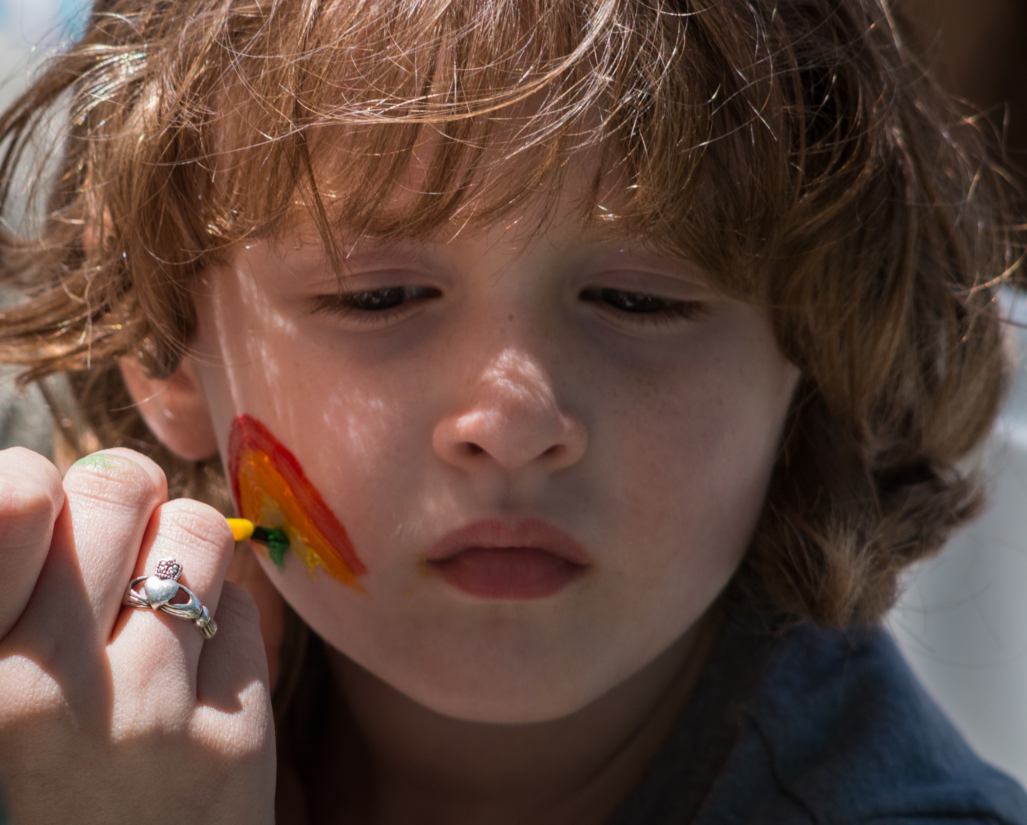 alt=Photo of a young child getting a rainbow painted on their face