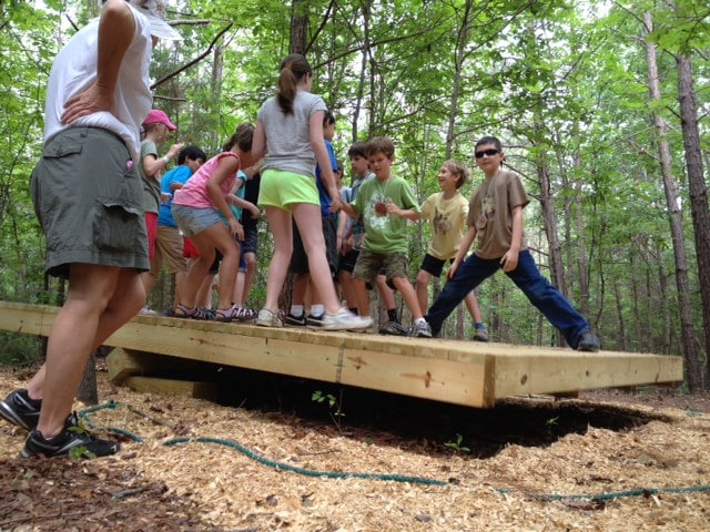 alt=Students standing on wood board in the woods of the Anne Springs Close Greenway
