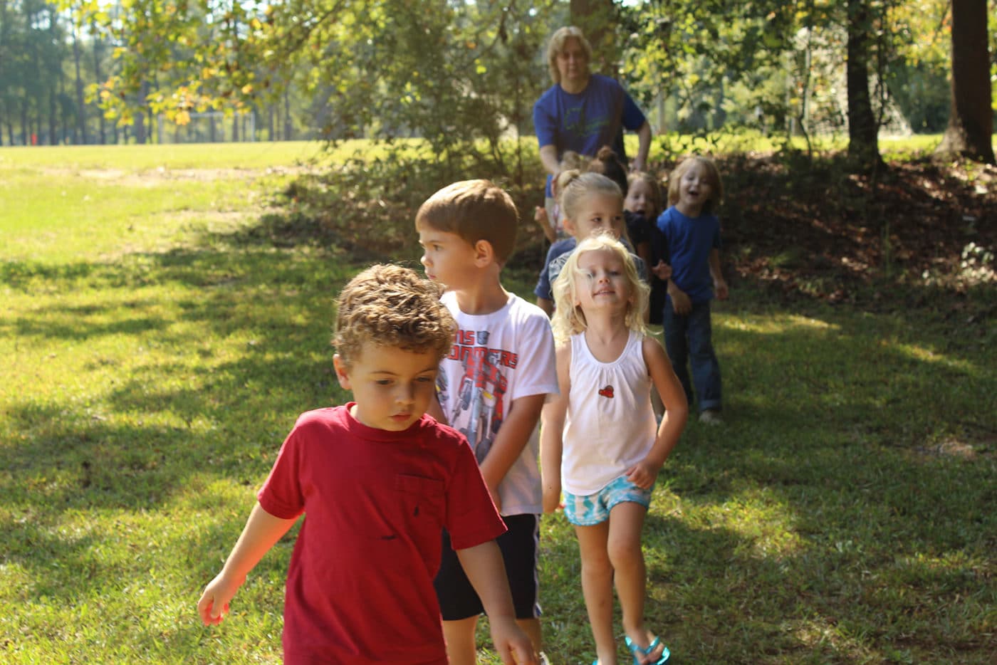 alt=Preschool students walking through the grass of the Anne Springs Close Greenway
