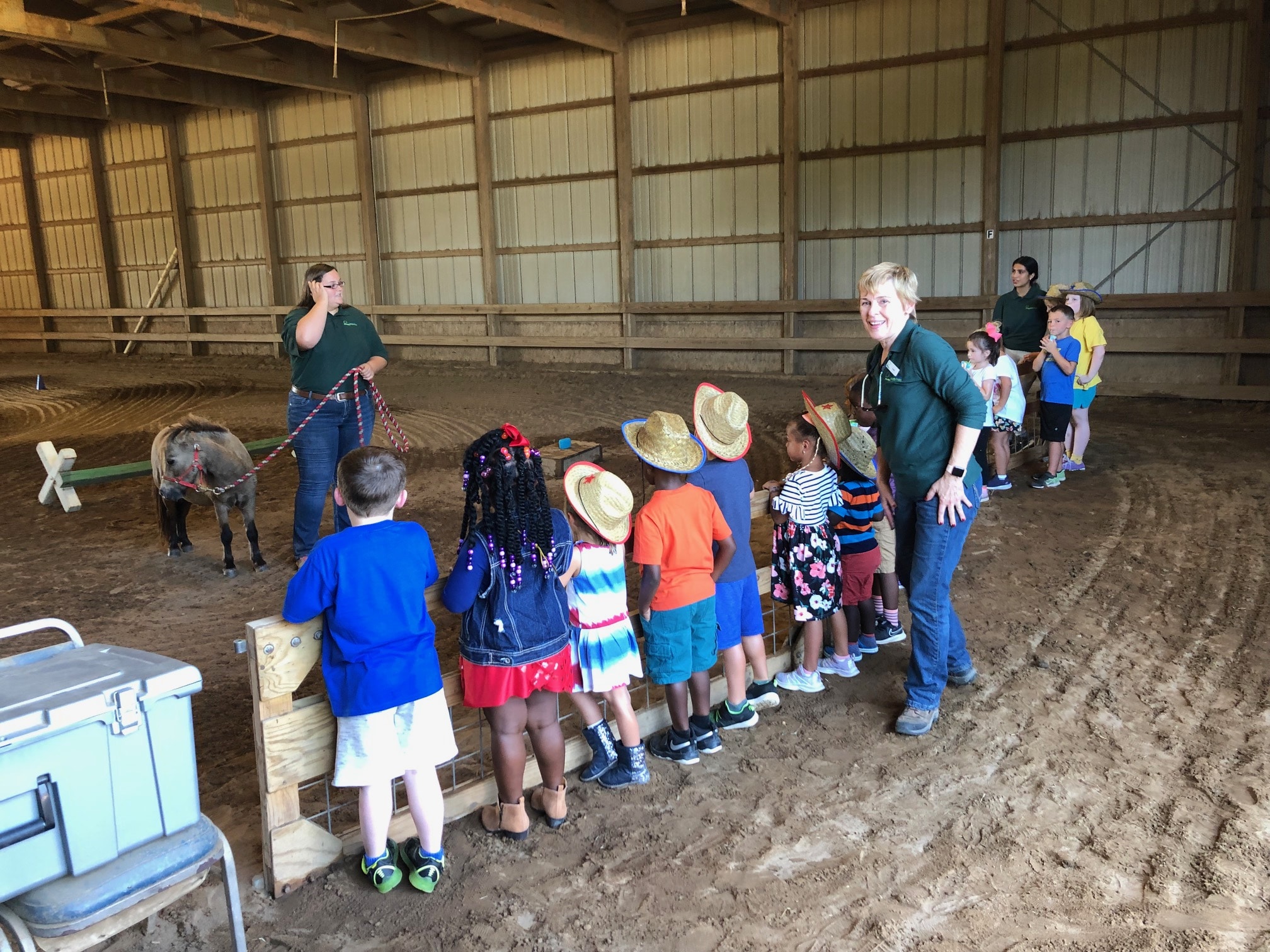 Photo of staff member holding pony while children stand behind fence