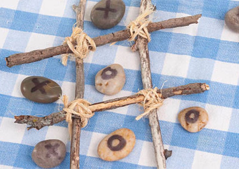 alt=Photo of sticks tied together to make a tic tac toe board with rocks marked X's and O's