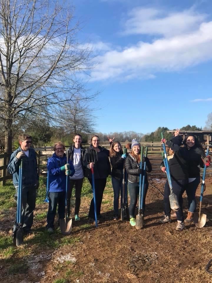 alt=Photo of volunteers posing with shovels at the Greenway Stables at the at the Anne Springs Close Greenway