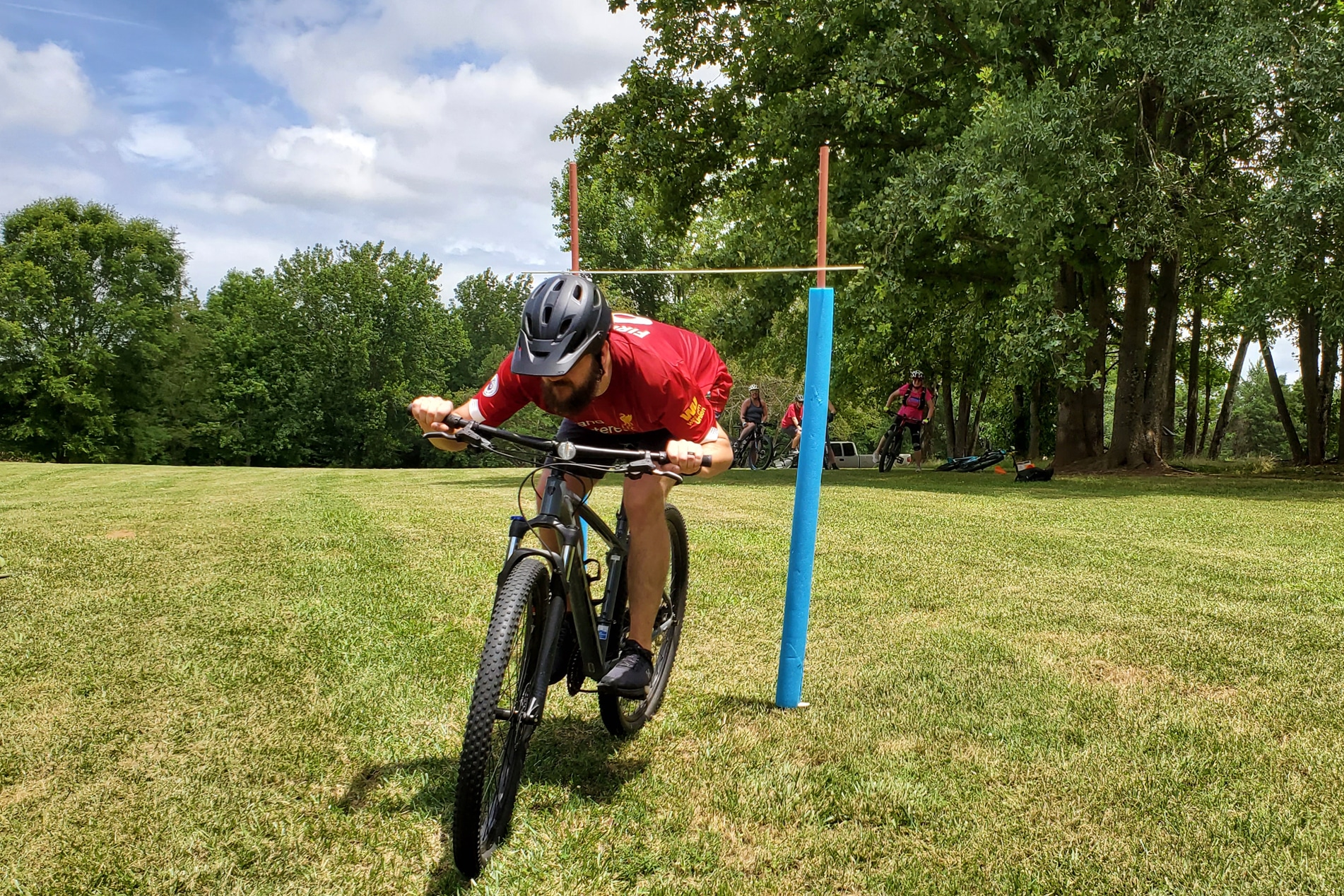 Photo of man crouching under hurdle on a mountain bike during the Level 1 Mountain Bike Clinic Evening Series at the Anne Springs Close Greenway