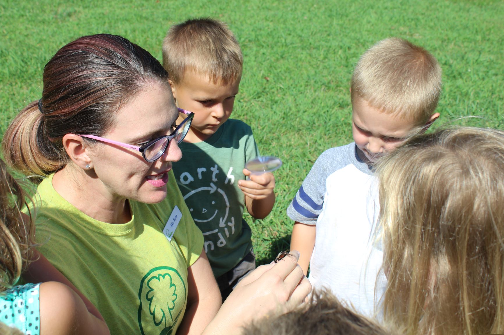 alt=Photo of Anne Springs Close Greenway Summer Camp counselor talking to children while holding a beetle
