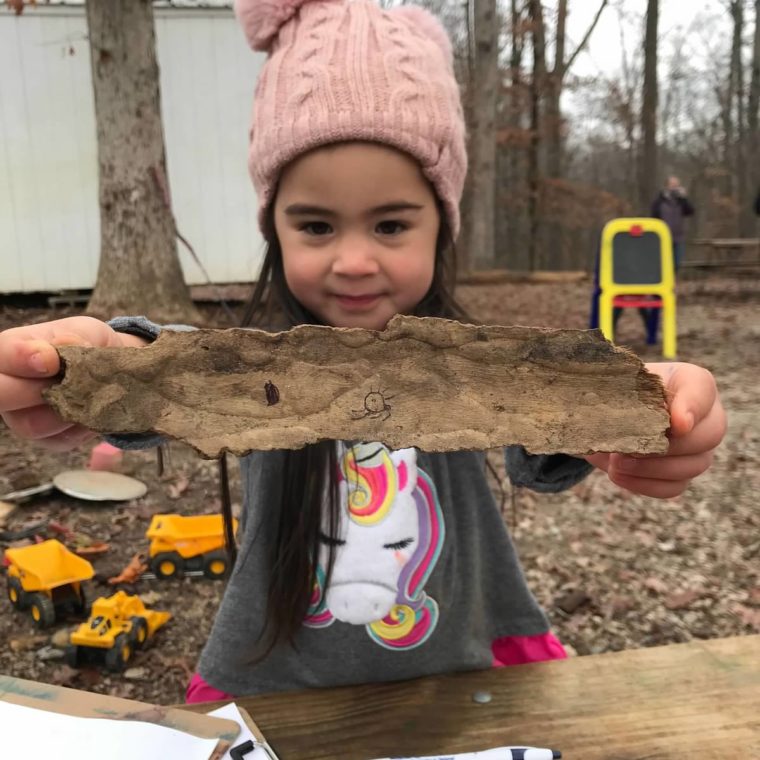 alt=Photo of young girl holding a piece of bark at the Anne Springs Close Greenway