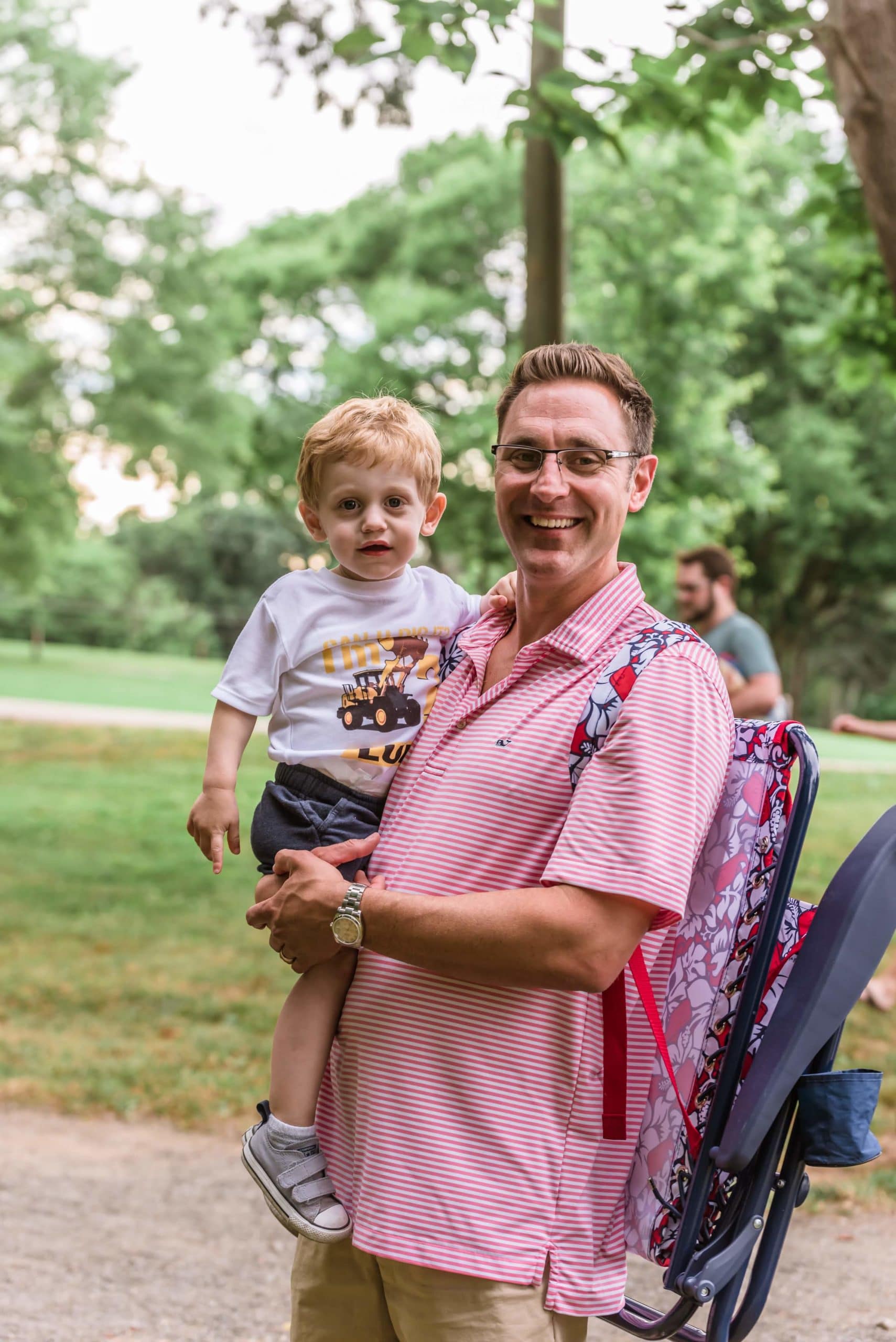 Photo of father holding young son while both smile at the camera at Anne Springs Close Greenway's Father's Day BBQ