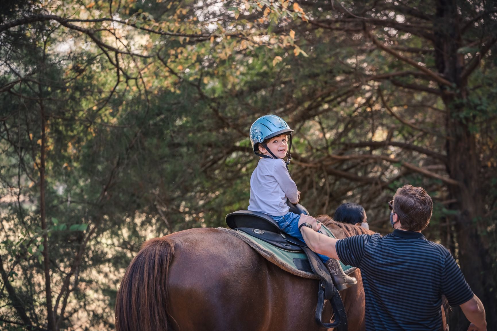Photo of young boy looking backwards smiling at the camera while riding a horse at the Anne Springs Close Greenway