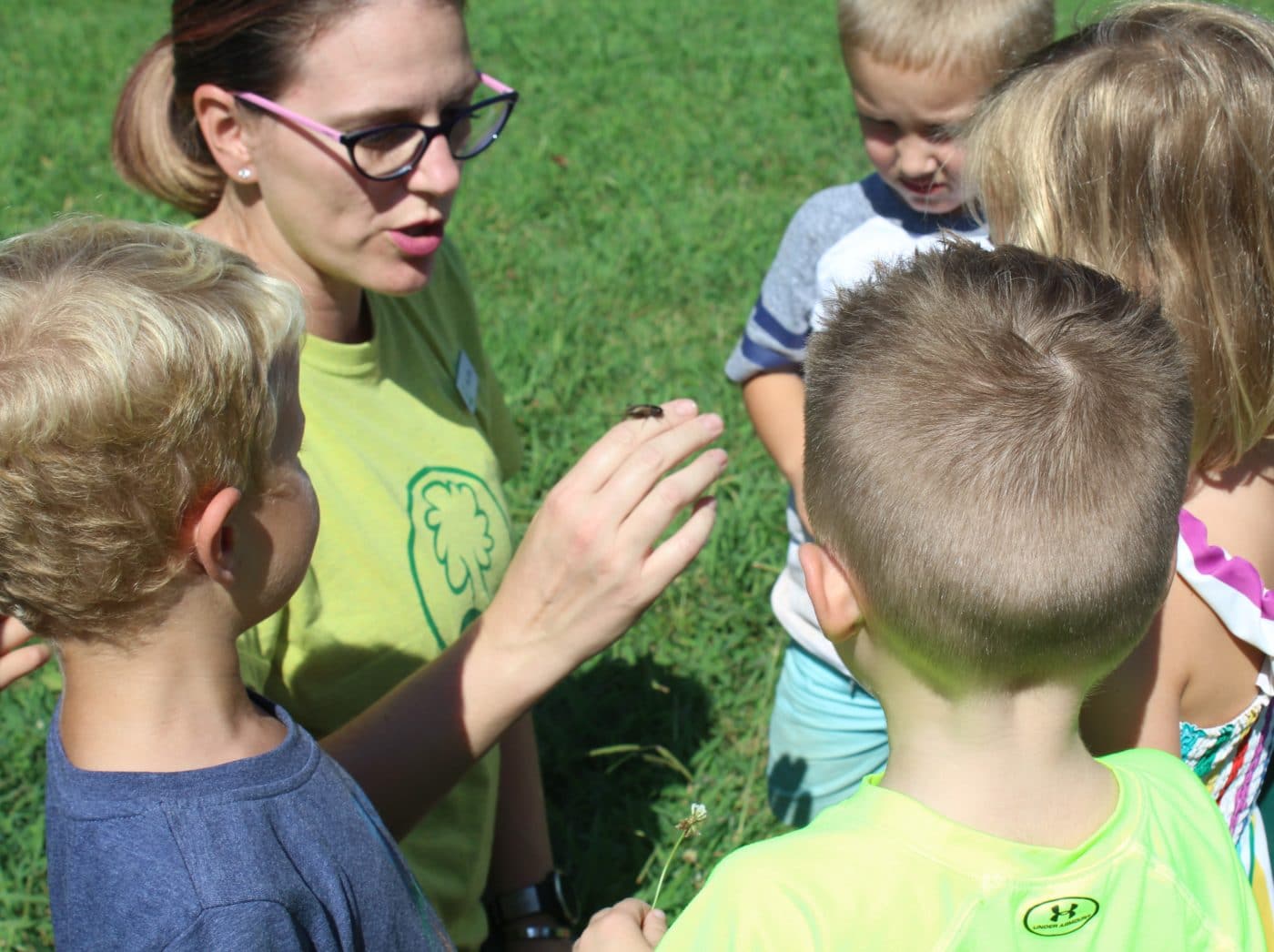 Photo of teacher speaking to 4 young students while holding a beetle at the Nature Based Preschool at Anne Springs Close Greenway