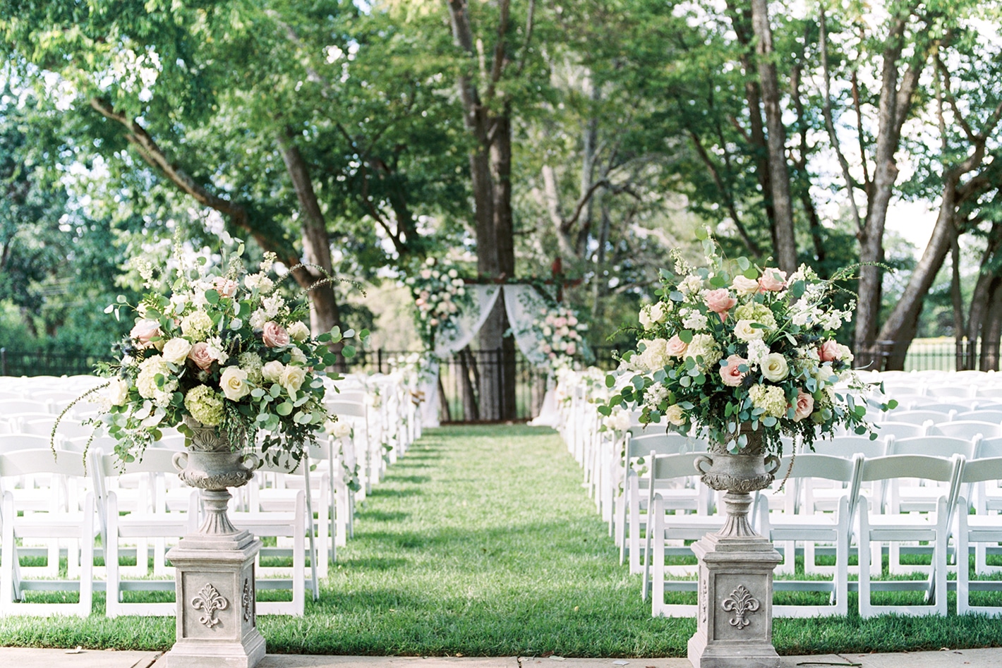 alt=Flowers and chairs framing the aisle of a wedding at the Anne Springs Close Greenway
