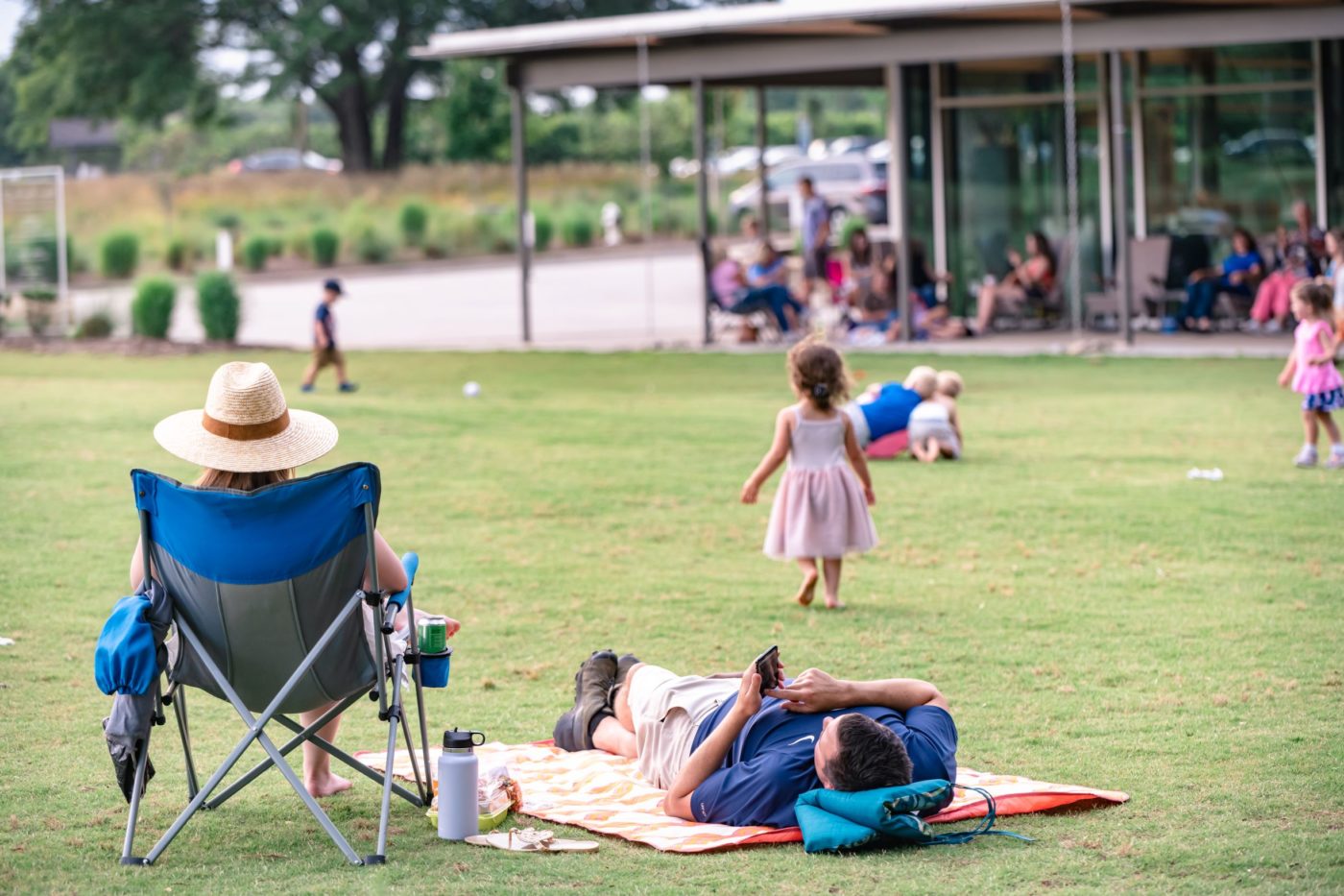 Photo of a mother sitting in a lawn chair, father laying on the grass, and child walking in the grass at the Gateway Lawn at the Anne Springs Close Greenway