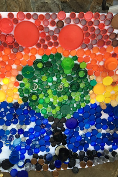 Close-up photo of a group of colorful plastic caps resembling a tree against a sunset sky.