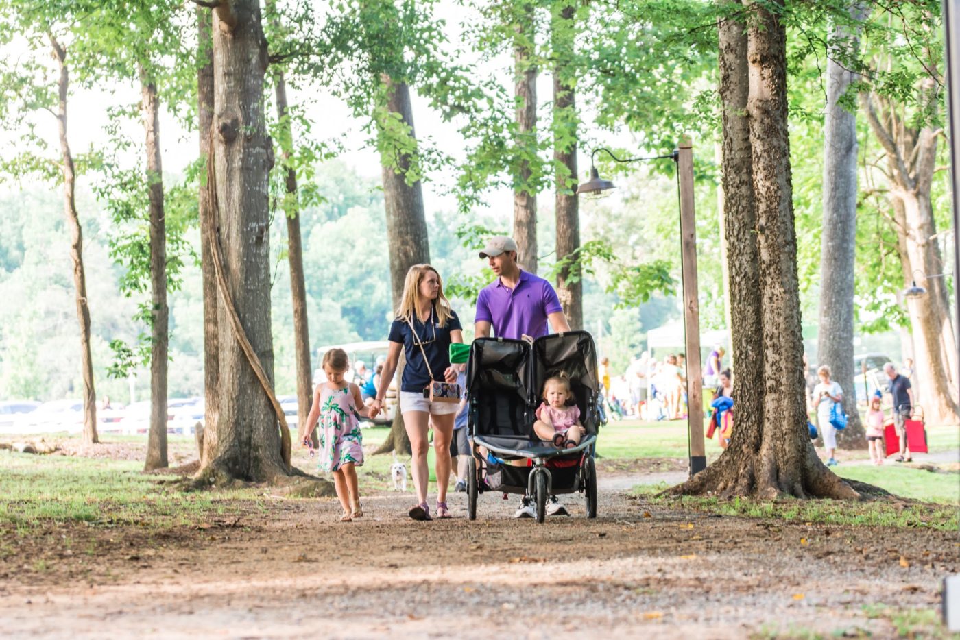 alt=Photo of mother holding daughter's hand while looking at father, who is pushing younger daughter in stroller