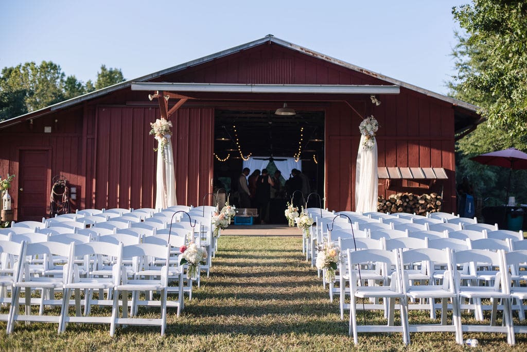 alt=Photo of white chairs set up out front of a barn at the Anne Springs Close Greenway