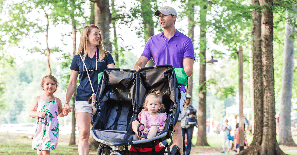 Mother holding hands with her older daughter and father pushing younger daughter in a stroller at the Anne Springs Close Greenway.