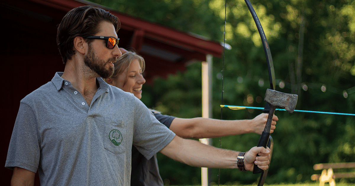 alt=Photo of a man holding an axe and a woman holding a bow and arrow