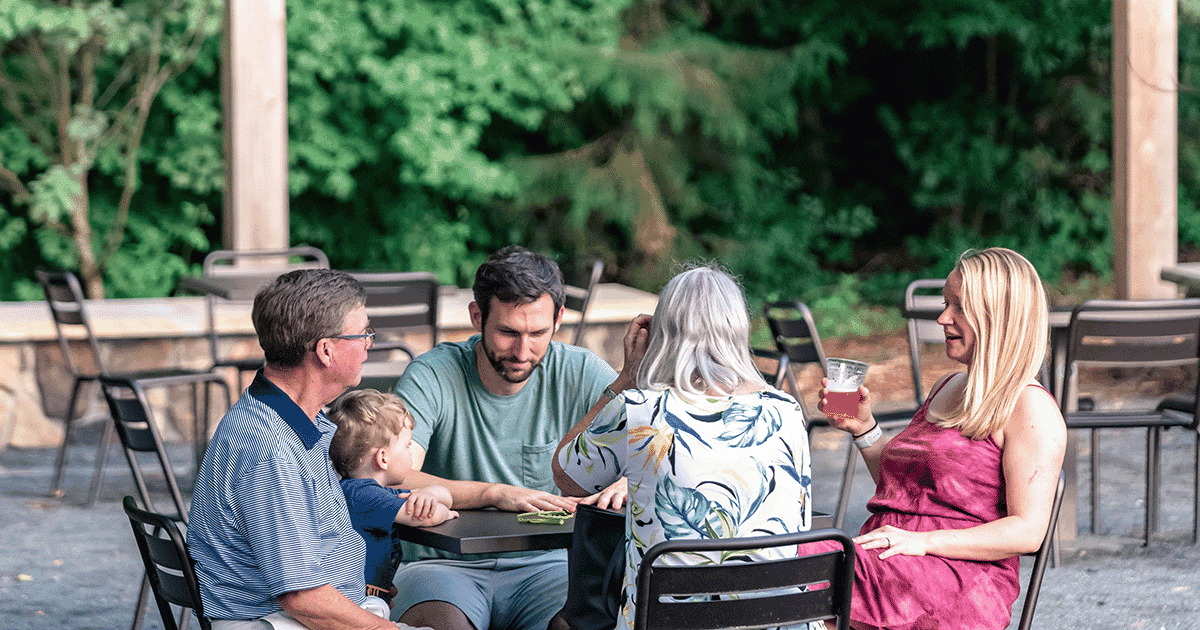 A family of 5 sitting at an outdoor table conversing at the Greenway Canteen.