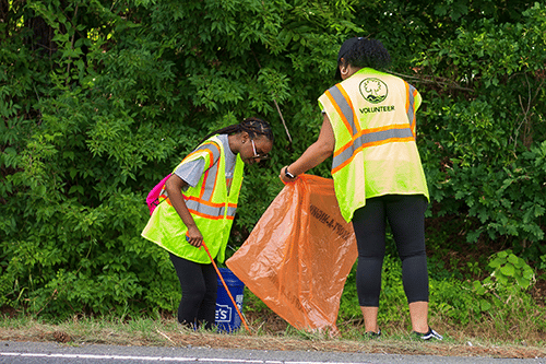 Photo of 2 women participating in litter clean up on the side of the Anne Springs Close Greenway