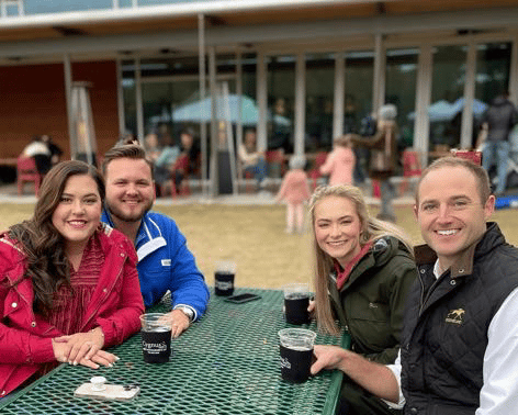 alt=Photo of guests sitting a table smiling at the camera while holding a beer at Boil & Brew