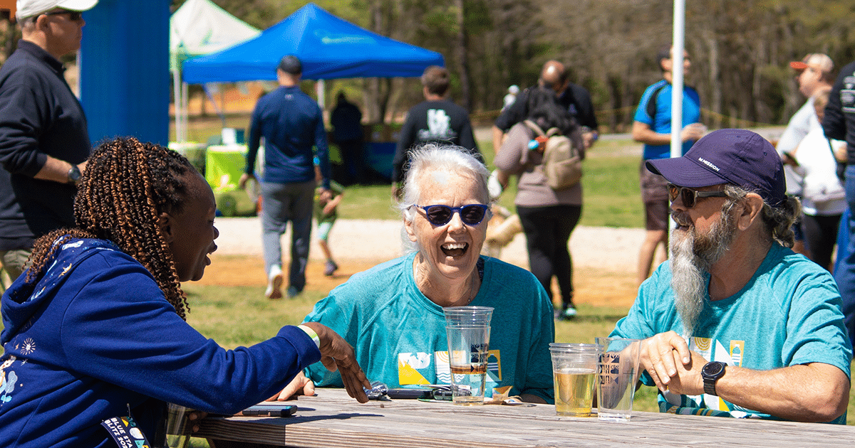 alt=Photo of people sitting at a bench laughing at the Blue Star Blitz Spring Festival