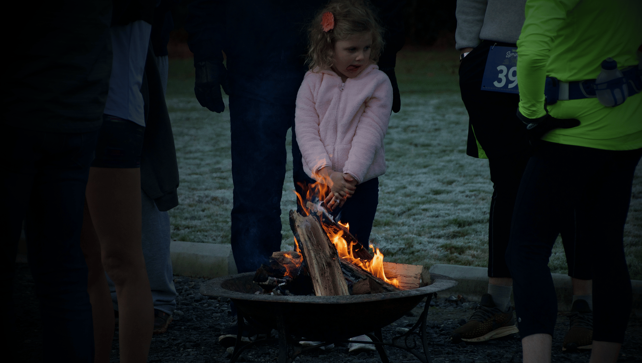 alt=Child standing by the fire at the Night Owl 5k at the Anne Springs Close Greenway