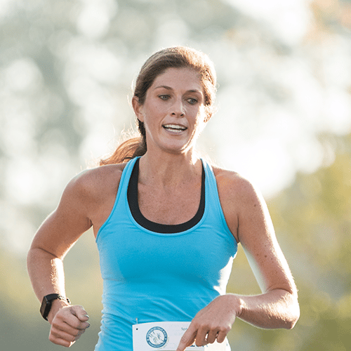 alt=Photo of woman crossing the finish line at the Springmaid Trail Race