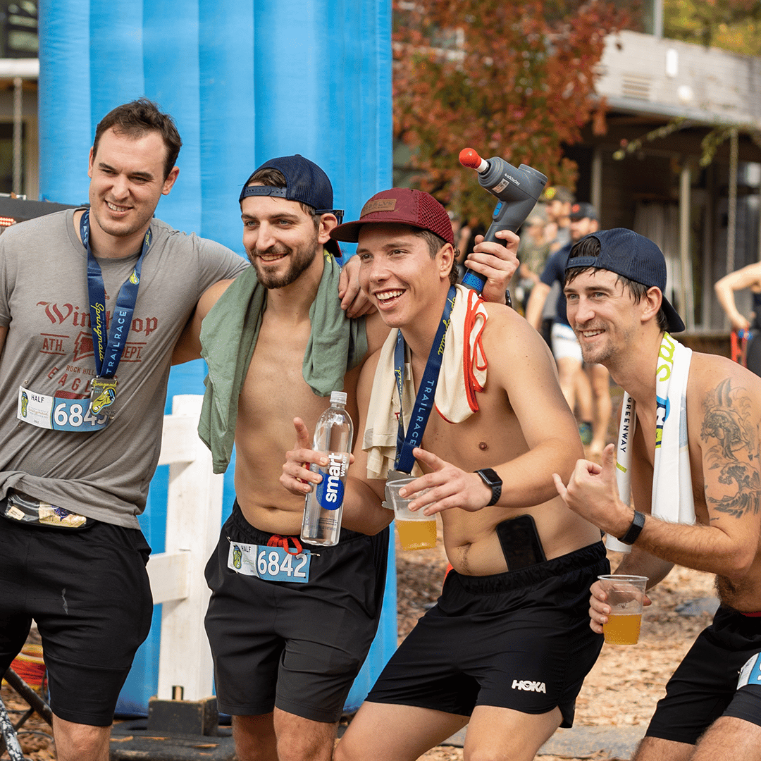 Photo of 4 men posing and smiling with medals and beer after the Springmaid Trail Run