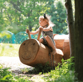 Little girl plays on snail-like natural play structure outdoors